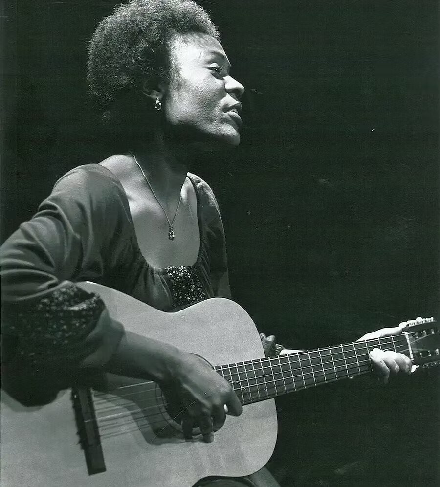Archive photograph of a singer with an acoustic guitar on the Black Ensemble stage
